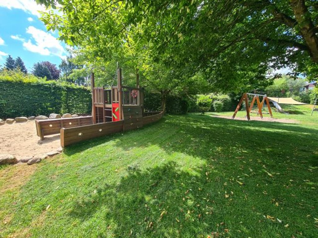 Außenbereich mit Holzschiff und Schaukeln der AWO Hamburg in der Kindertagesstätte Zauberburg.